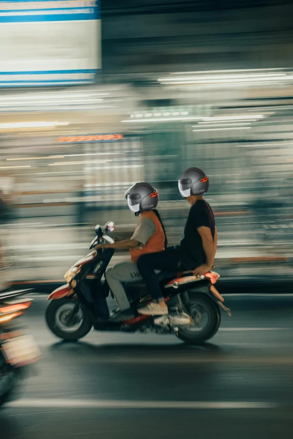 Two riders on a scooter at night wearing the helmet