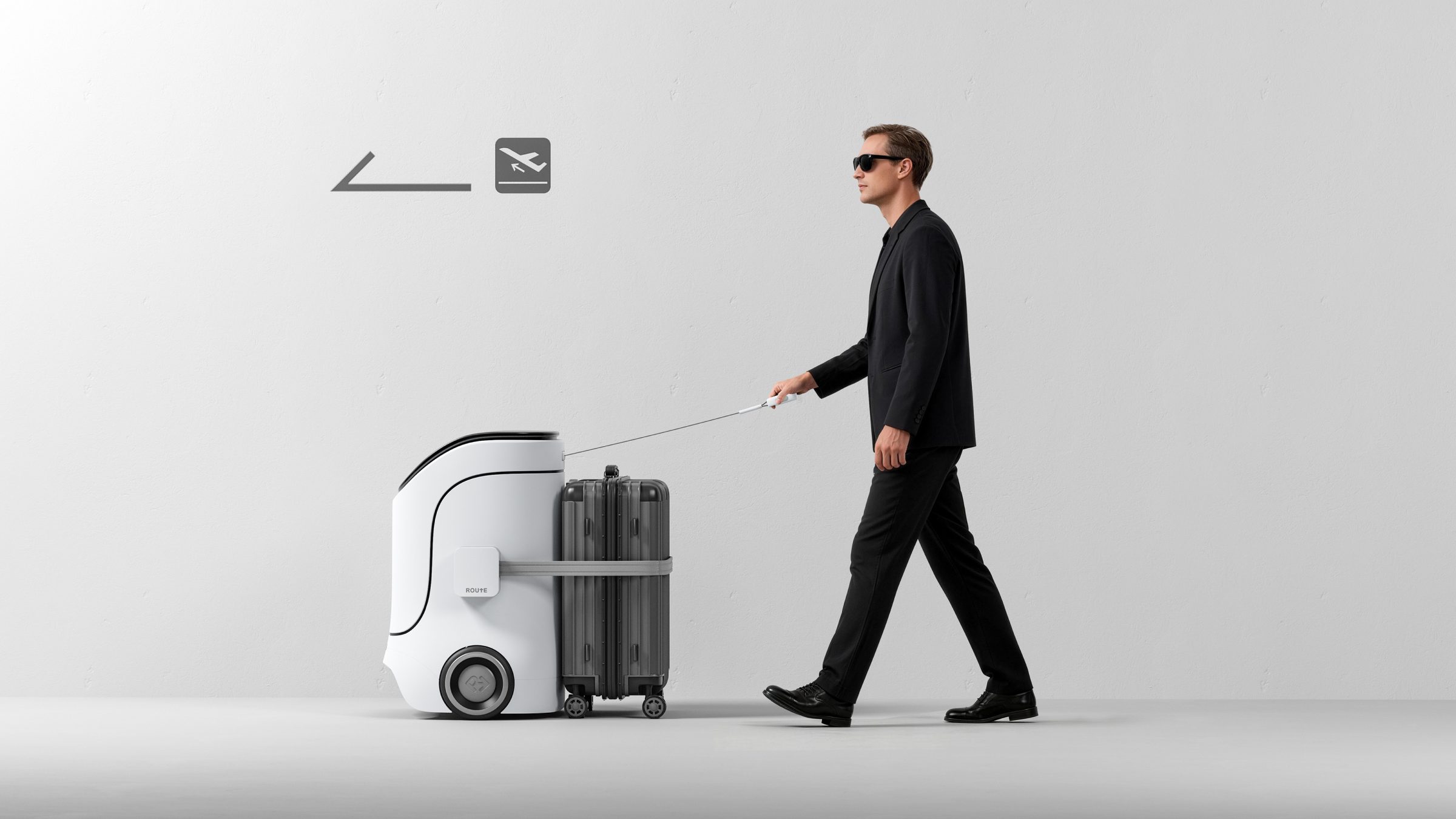A traveler in dark glasses holds ROUTE's handle line while it tows his suitcase toward the departures sign