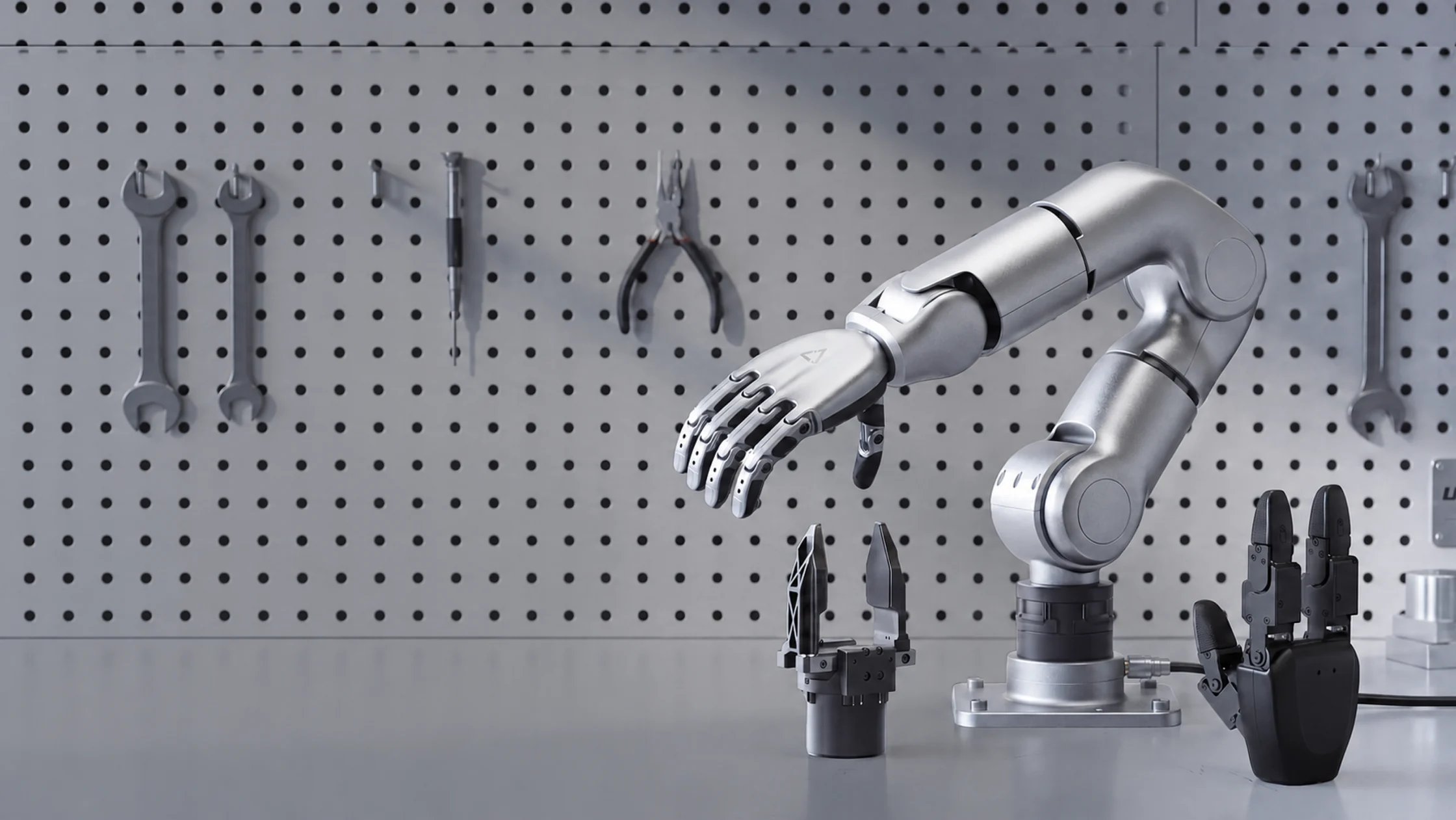 A silver D2 arm with a robotic hand at a workbench, two grippers on the table beside it